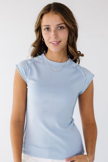 Young woman wearing  a light blue rib knit top with a high round neckline, exposed seams and short raglan sleeves of a smooth fabric and rolled hems.