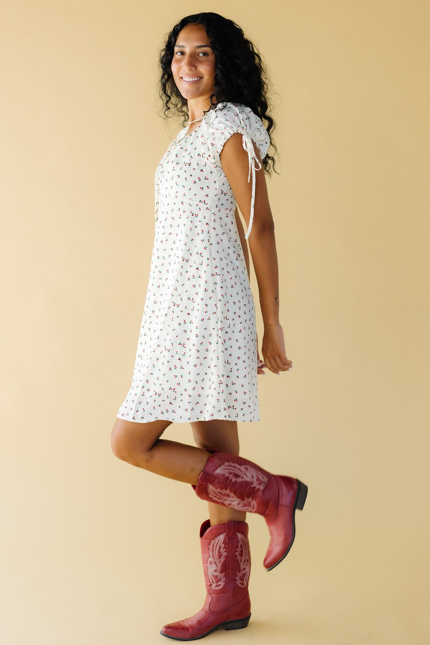 Side view of a woman wearing a cream and red floral print dress with short puff sleeves and a ties cuff.