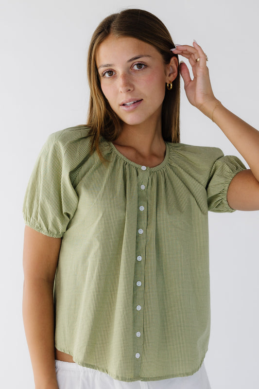 Young woman wearing a modest loose fitting green gingham blouse that buttons down the front with short puff sleeves.