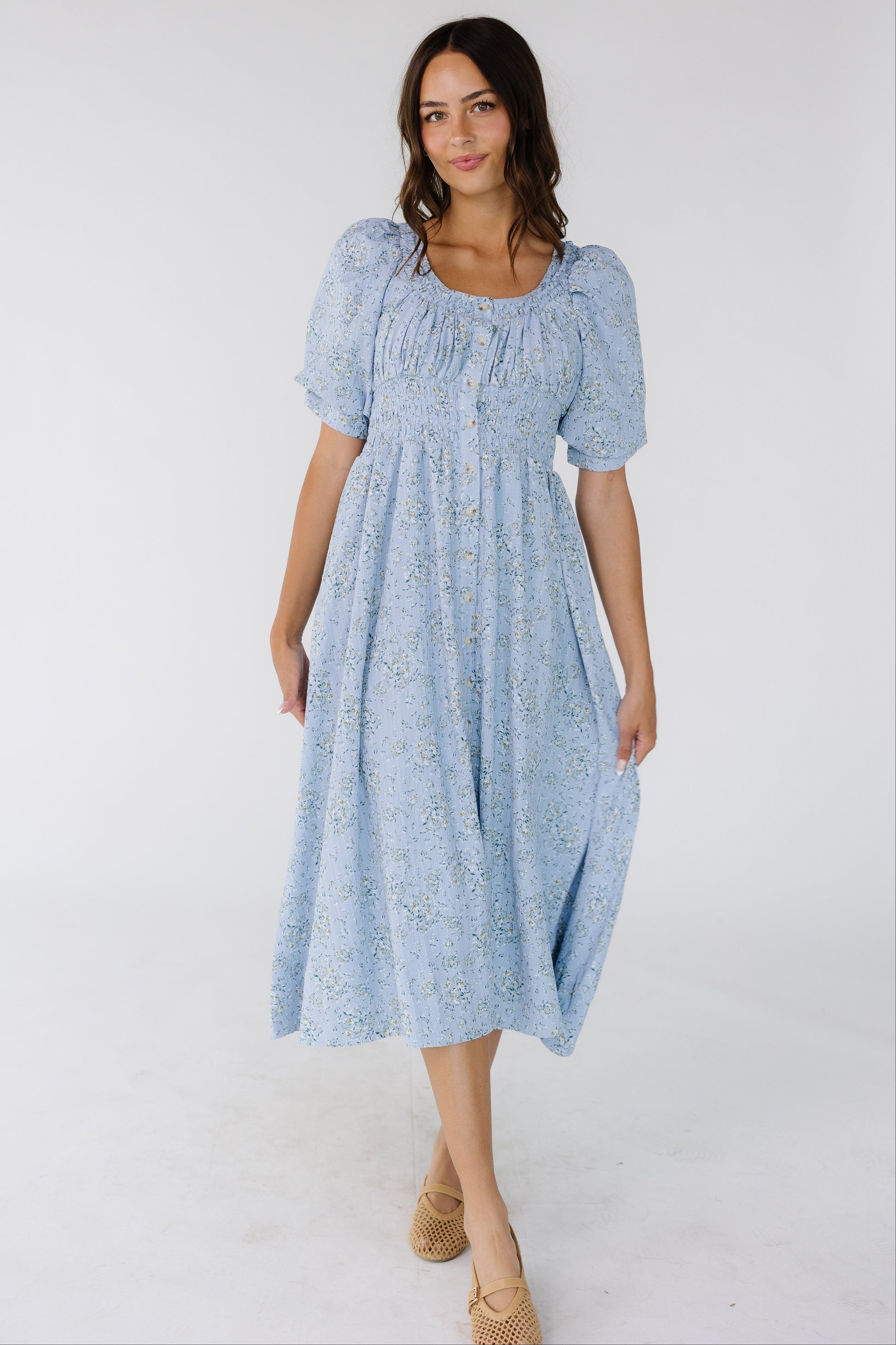 Woman wearing a blue floral button down dress with a scoop neckline, large puff sleeves and a full skirt.