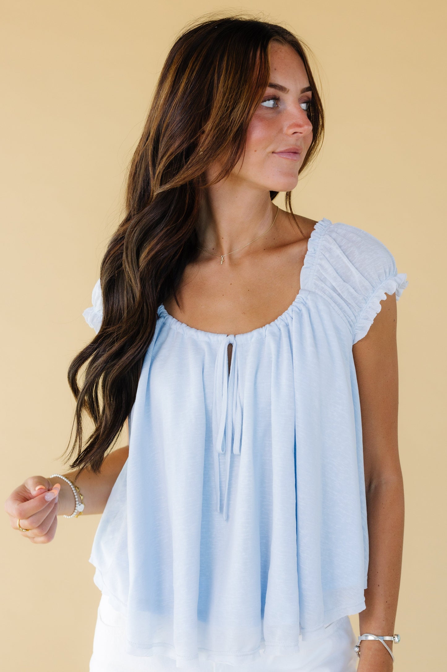 Woman wearing a loose fitting light blue blouse with gathered cap sleeves and a drawstring scoop neckline.