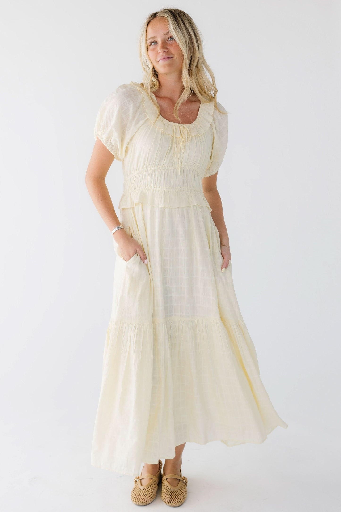 Young woman wearing a light yellow midi-maxi dress with side pockets and a close fitting bodice and wide waist.