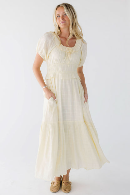 Young woman wearing a light yellow midi-maxi dress with side pockets and a close fitting bodice and wide waist.