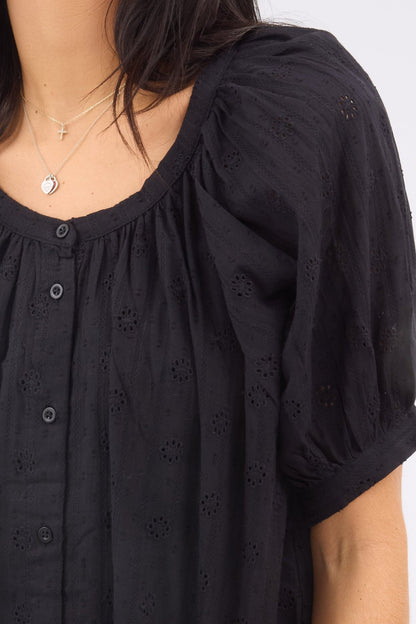 A close view of a woman wearing a black eyelet button down blouse with a round neckline and short puff sleeves.