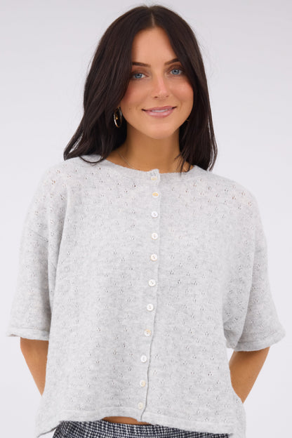 A young woman wearing a modest loose fitting pointelle knit cardigan with short sleeves in light grey.