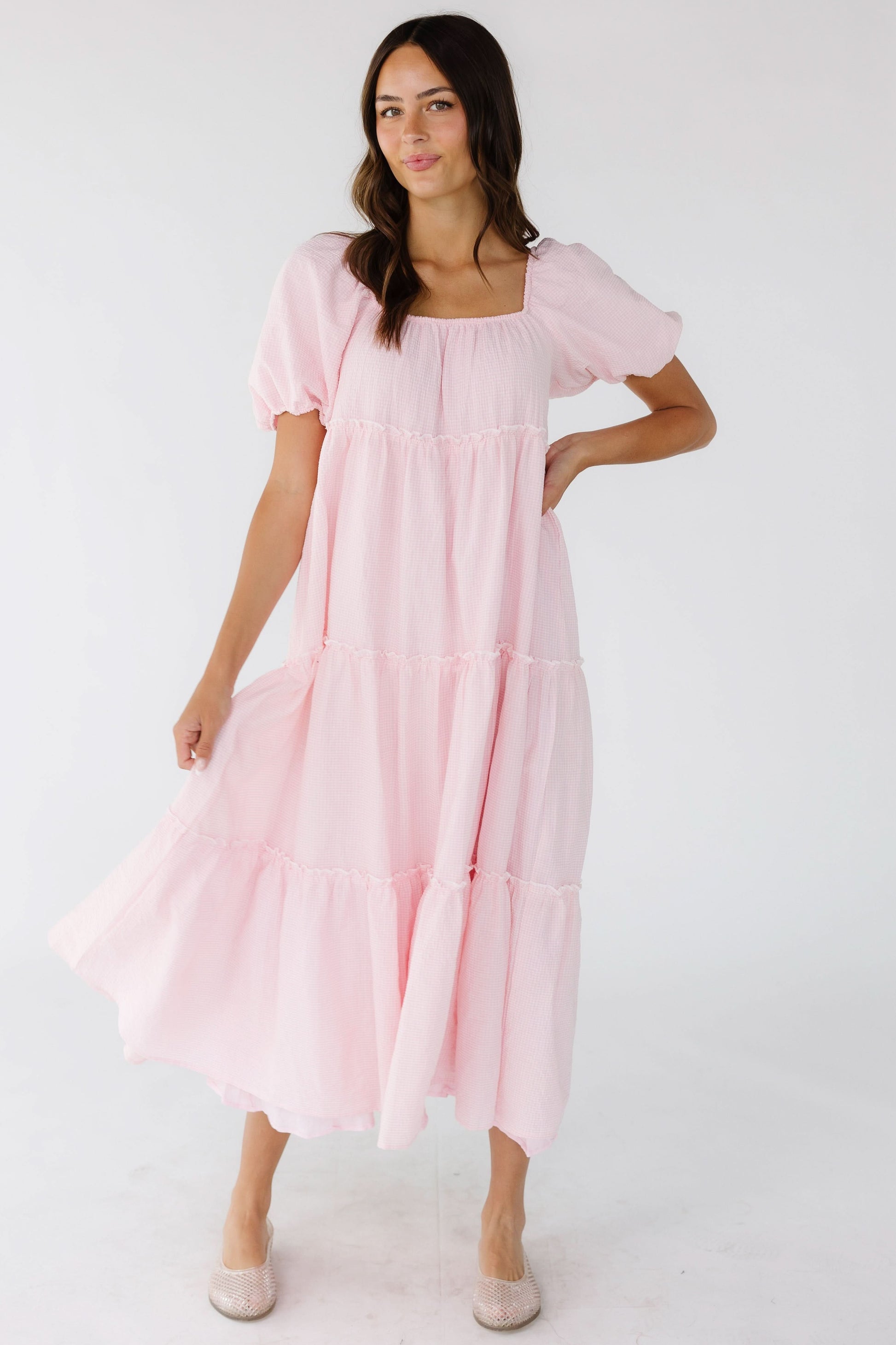 Young woman wearing a pink gingham tiered midi dress with a square elastic neckline and balloon sleeves.