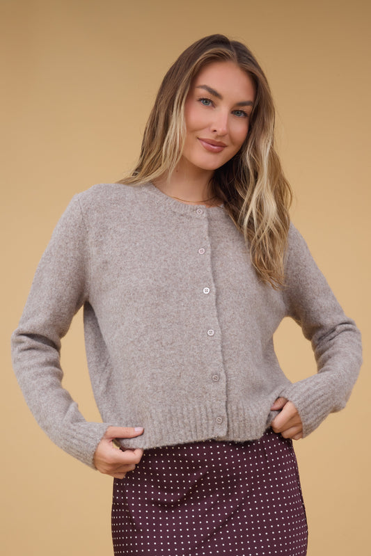 A young woman wearing a modest beige button down cardigan with matching buttons and long sleeves.