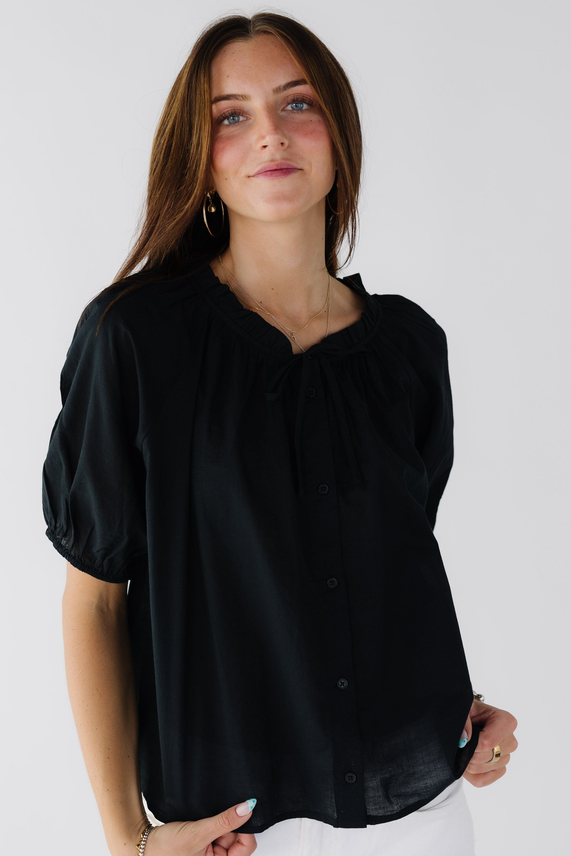 Woman wearing a loose fitting button down blouse with shortgathered sleeves and a ruffle collar.