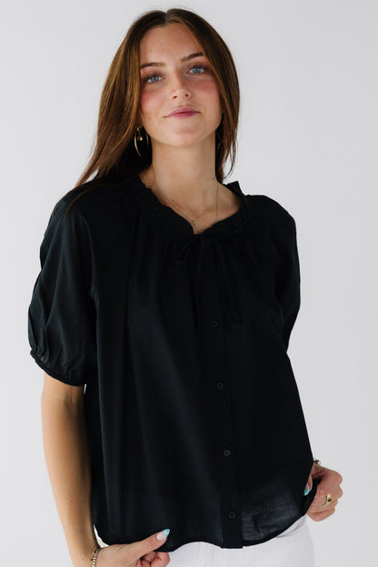 Woman wearing a loose fitting button down blouse with shortgathered sleeves and a ruffle collar.