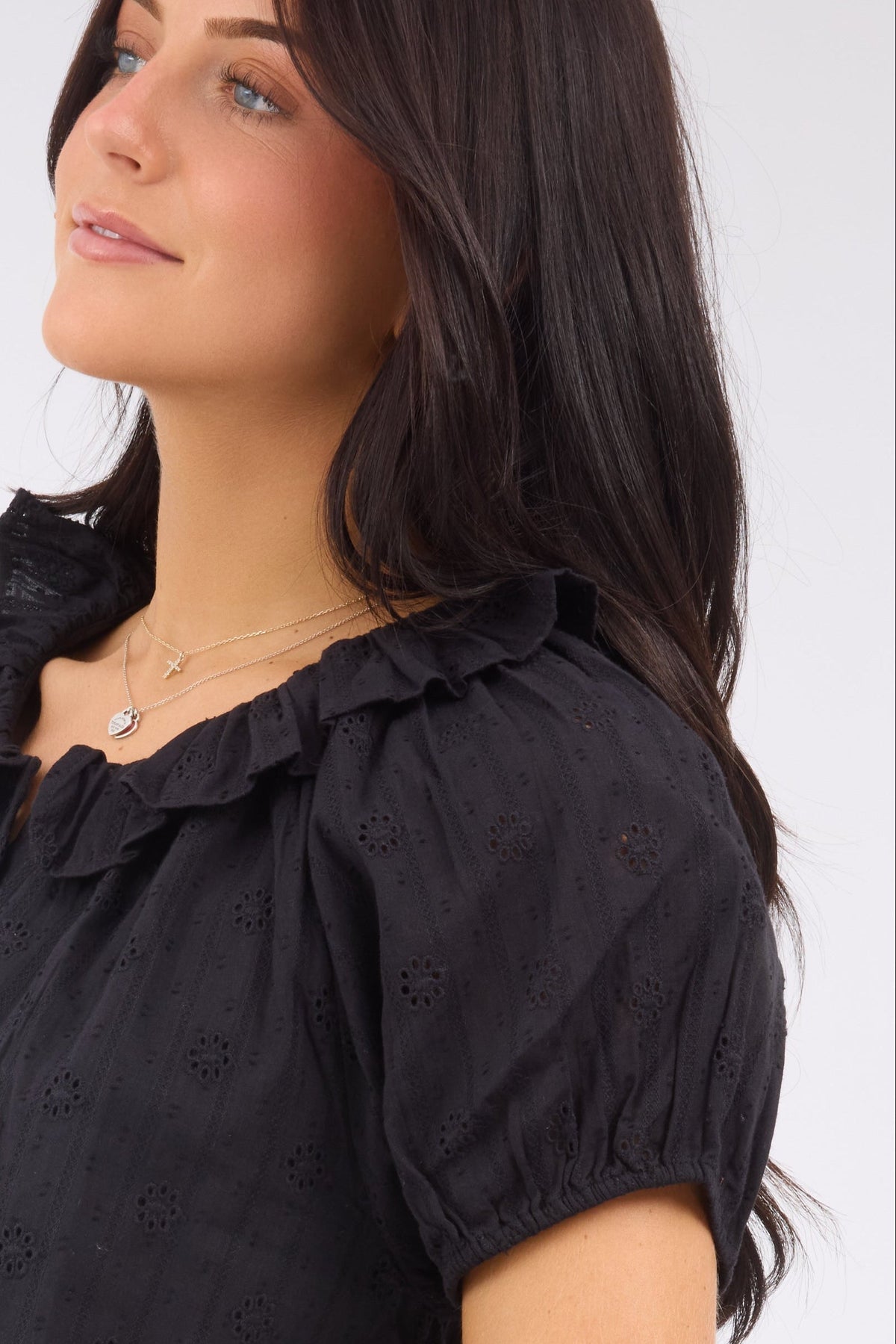 A close up view of a woman wearing a black eyelet blouse with shrot puff sleeves and a round ruffle neckline.