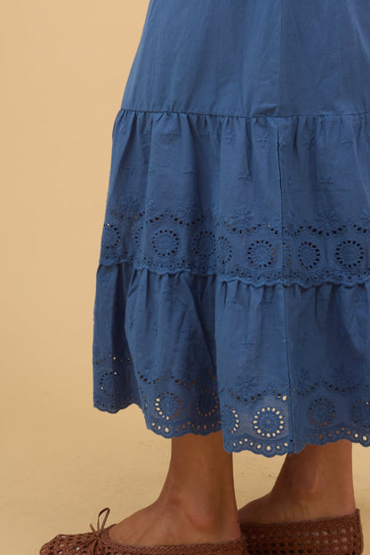 Close view of a woman wearing a blue midi skirt with a wide eyelet ruffle.