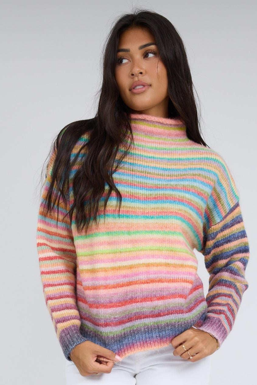 Woman wearing a rainbow stripe, long sleeve sweater with a mocke turtleneck.