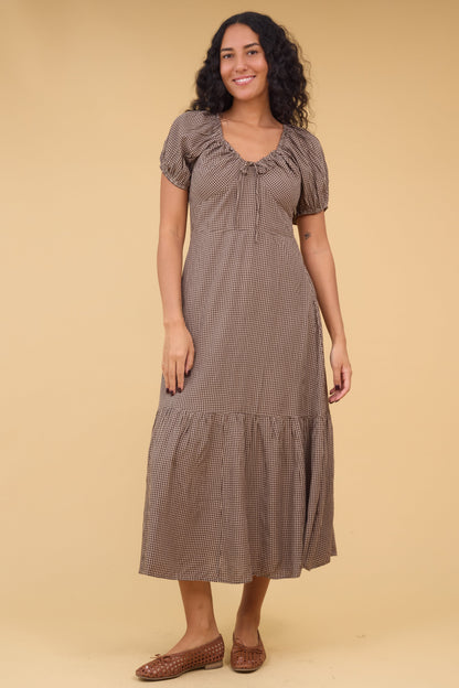 Woman wearing a brown gingham midi dress with a scoop drawstring neckline and short puff sleeves.