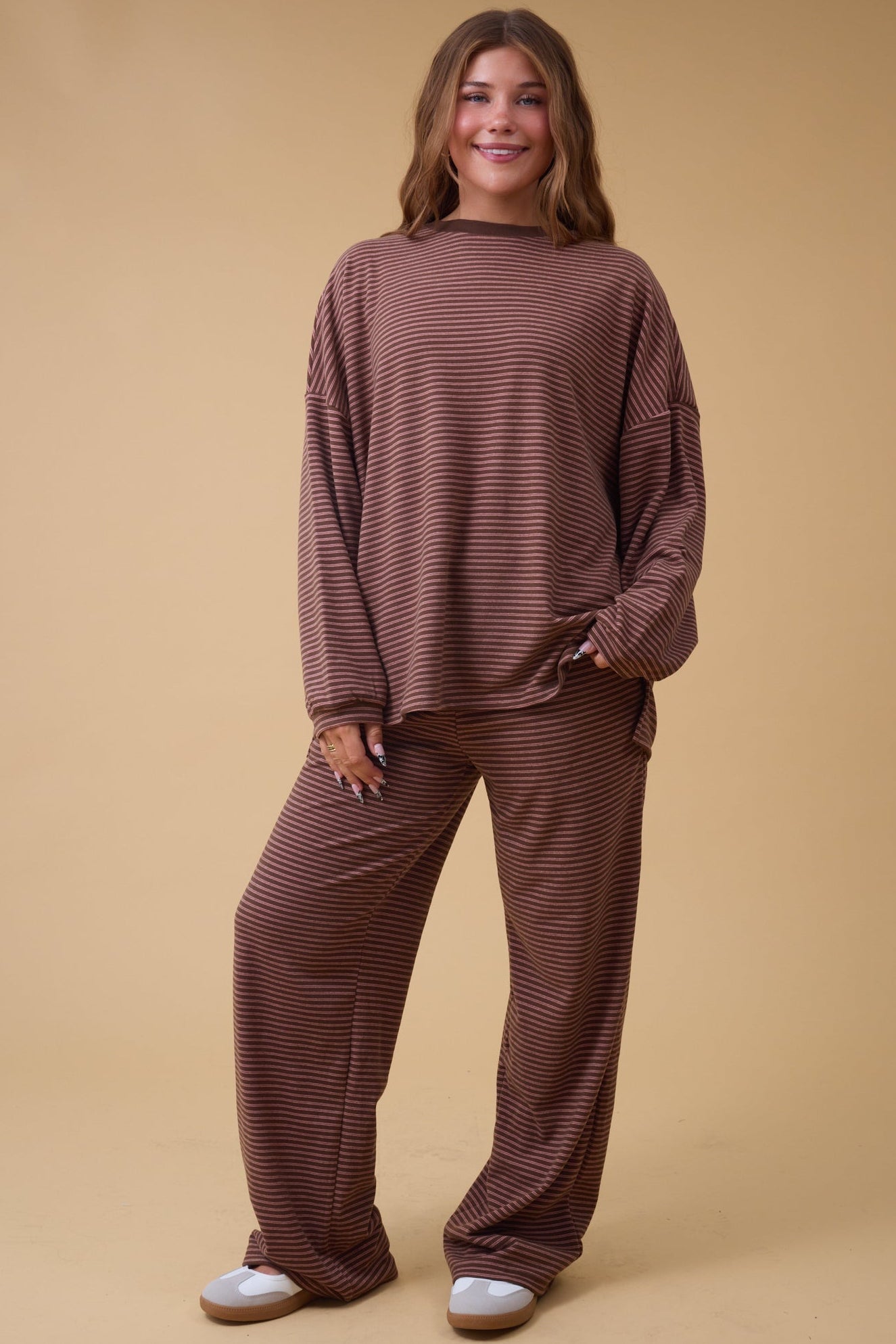 Young woman wearing a redish brown stripe lounge set with long sleeves and long pants.
