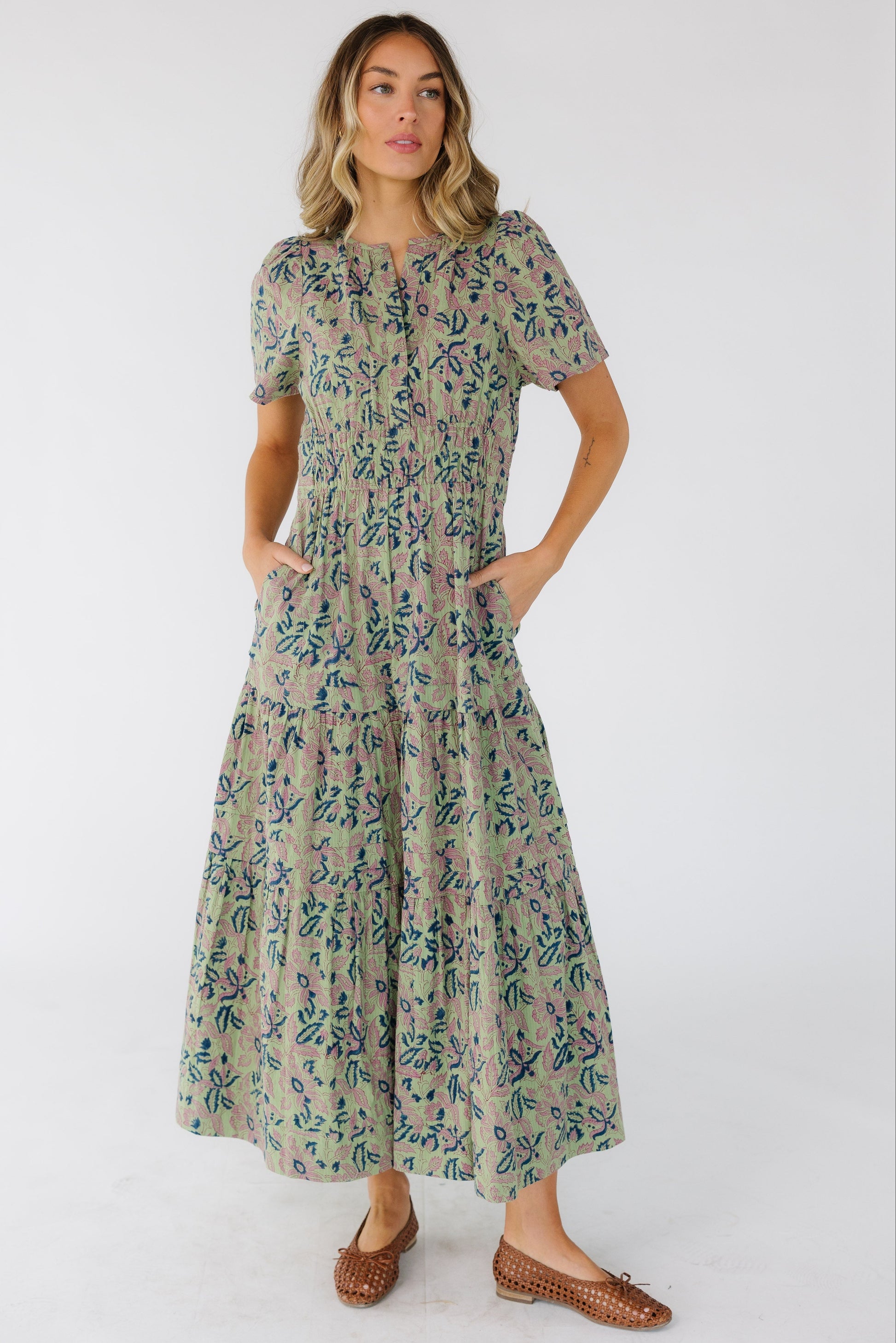 Woman wearing a green print midi-maxi dress with pockets, a wide waistband and short sleeves.