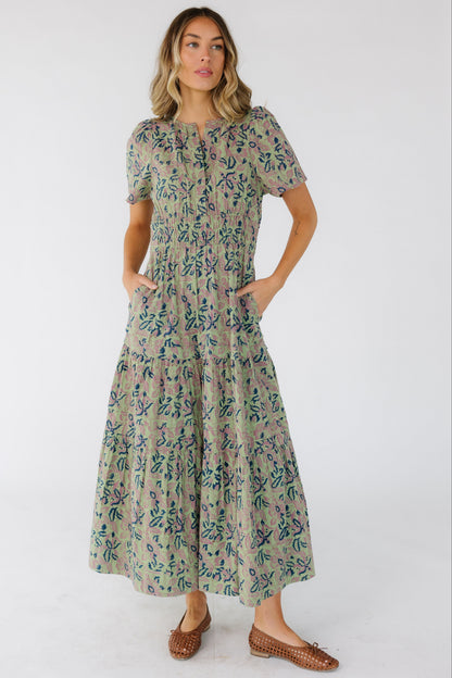 Woman wearing a green print midi-maxi dress with pockets, a wide waistband and short sleeves.
