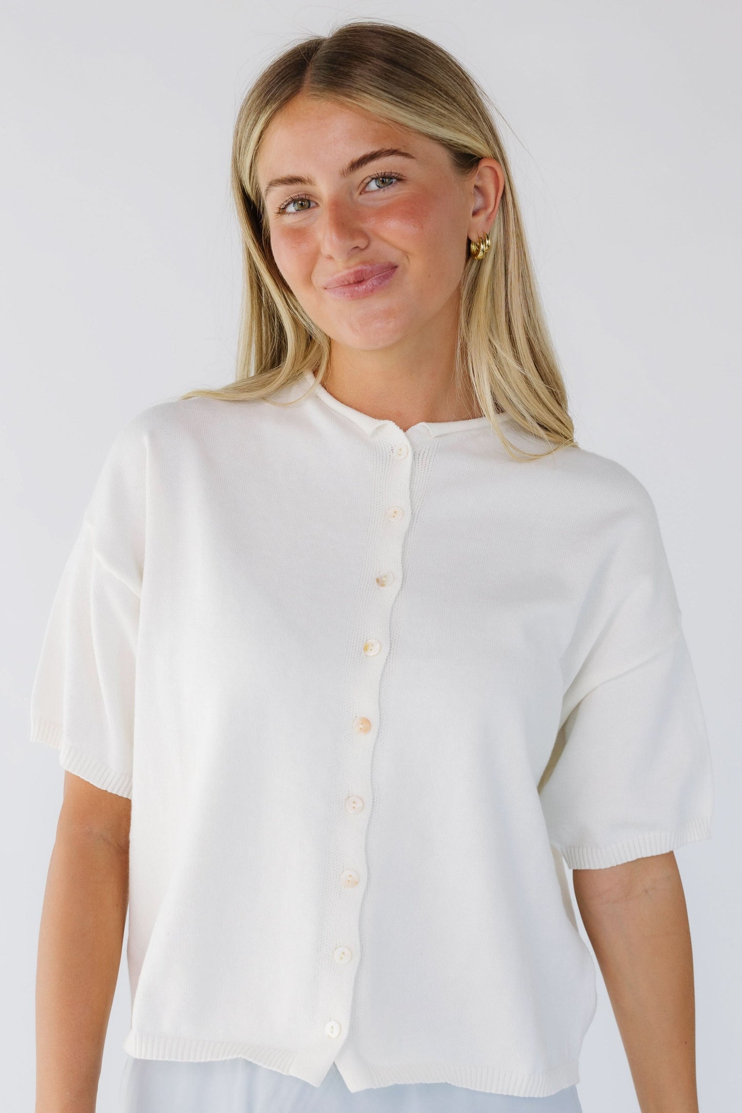 Young woman wearing a modest ivory button down cardigan with a rolled round neckline and short sleevs.