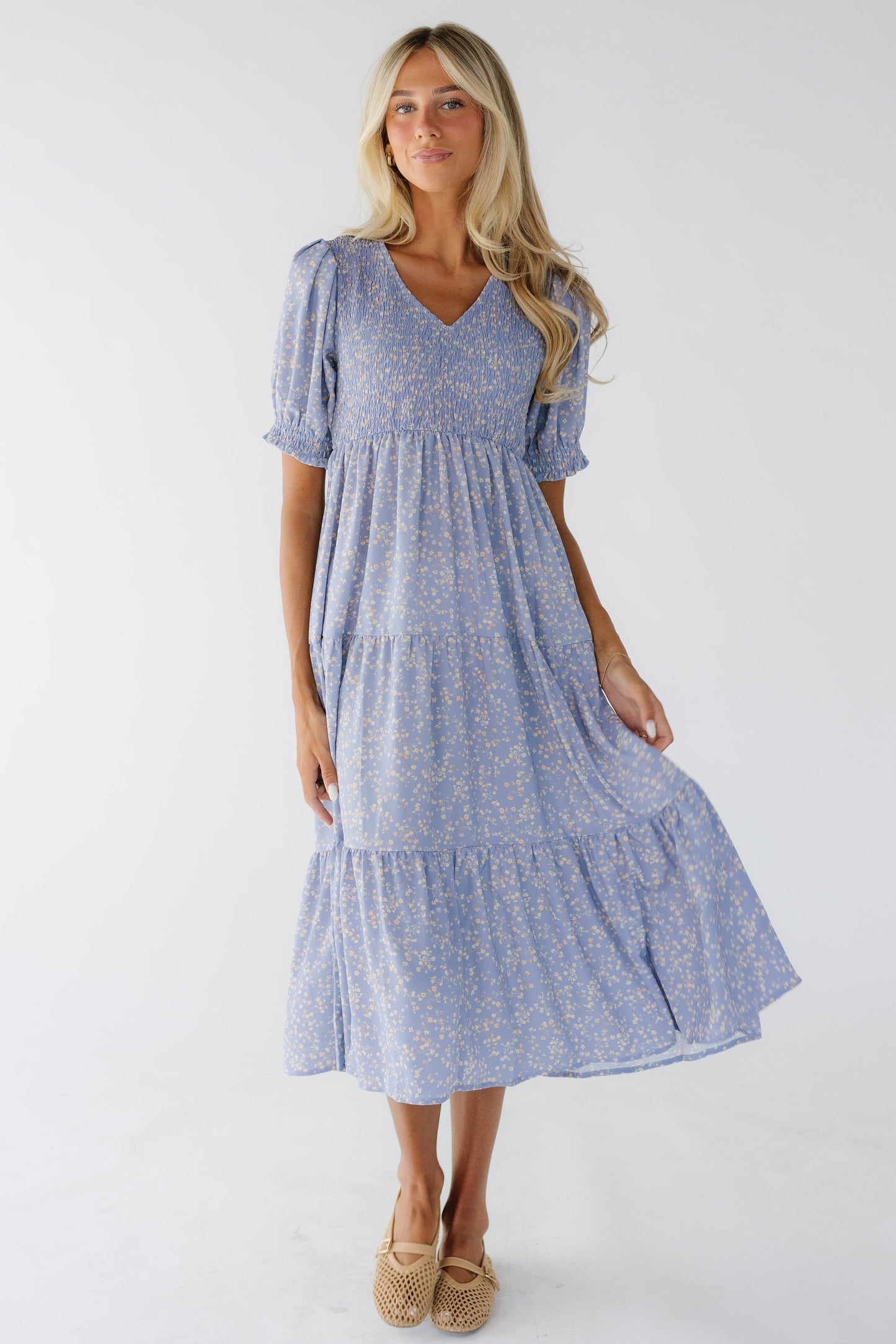 Woman wearing a light purple floral tiered midi dress with a smocked bodice, V-neckline and short puff sleeves with smocked cuffs.