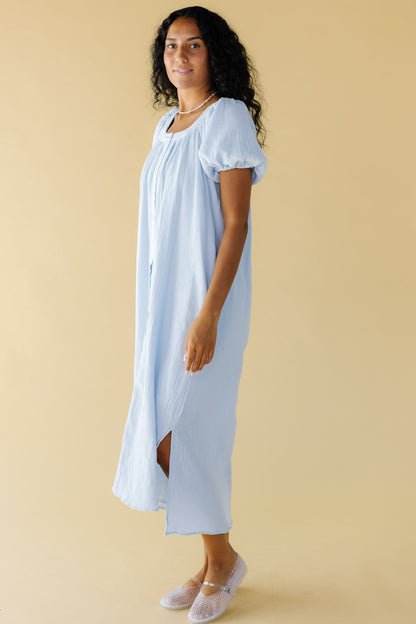 Young woman wearing a blue crepe textured midi dress that buttons down the front with balloon sleeves and a scoop neckline.