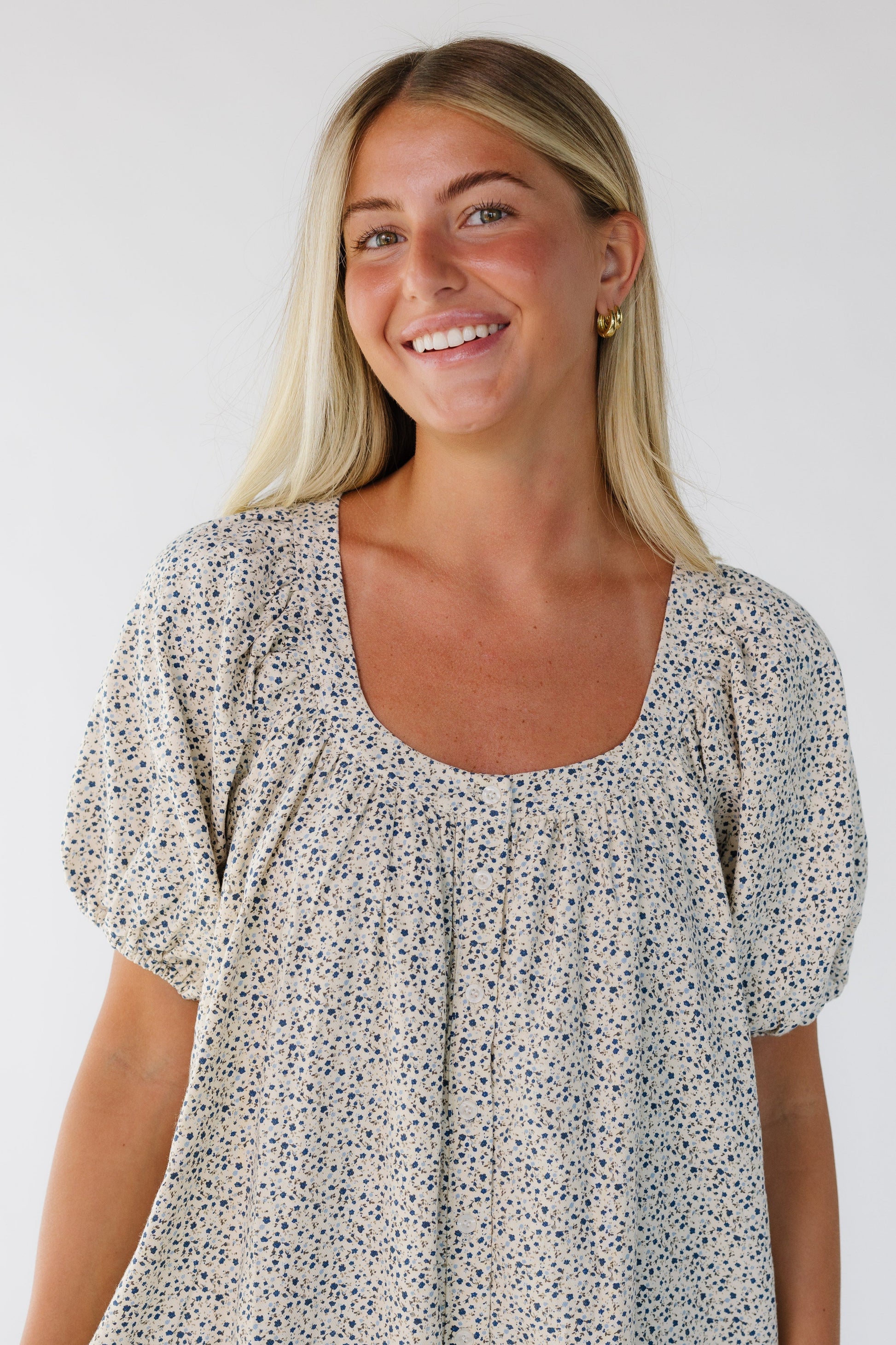 Woman wearing a cream and blue floral button down dress with a scoop neckline and balloon sleeves.
