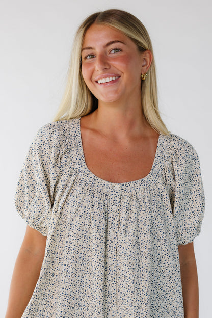 Woman wearing a cream and blue floral button down dress with a scoop neckline and balloon sleeves.