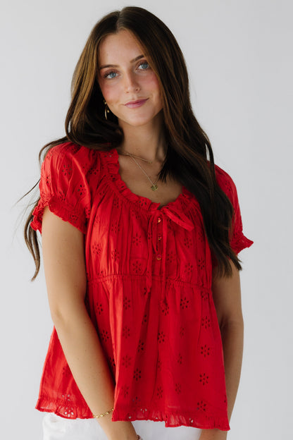 Young woman wearing a red eyelet blouse with short sleeves and a scooped ruffled neckline.