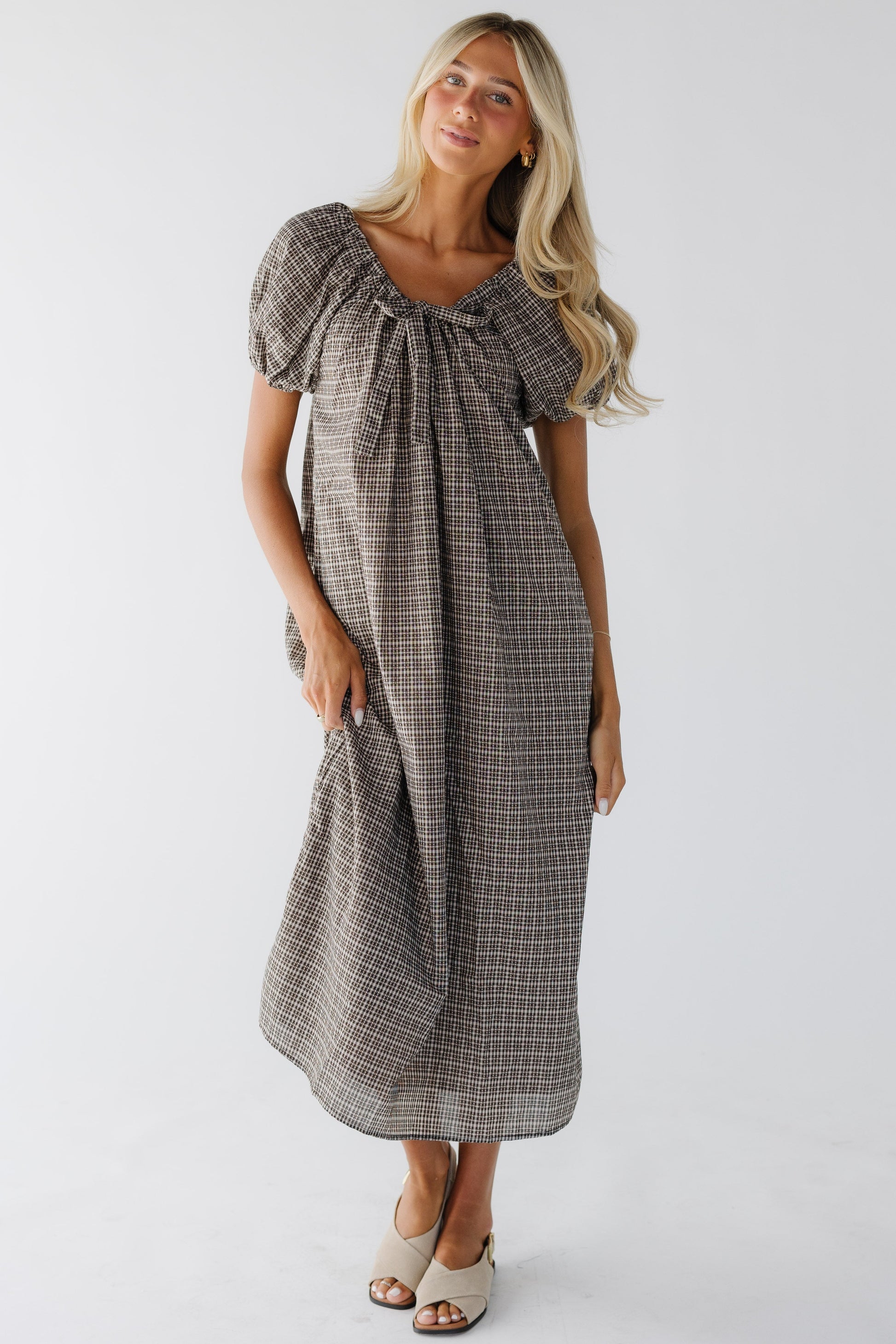 Woman wearing a black plaid loose fitting midi dress with large puff sleeves and a drawstring-scoop neckline.