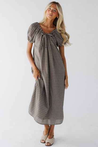 Woman wearing a black plaid loose fitting midi dress with large puff sleeves and a drawstring-scoop neckline.