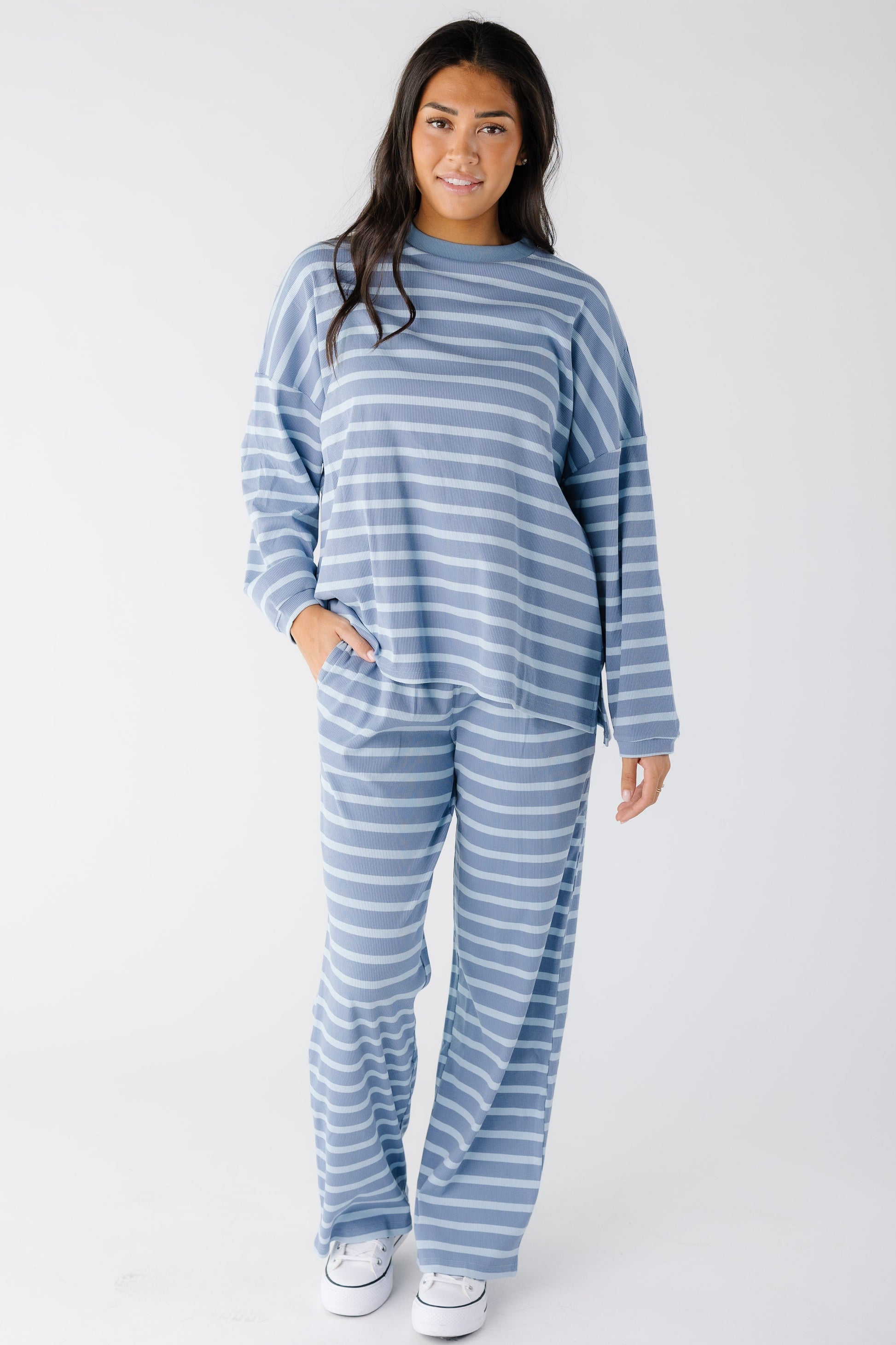 Young woman wearing a loose fitting lounge set in light blue stripe with long sleeves and long wide leg pants.