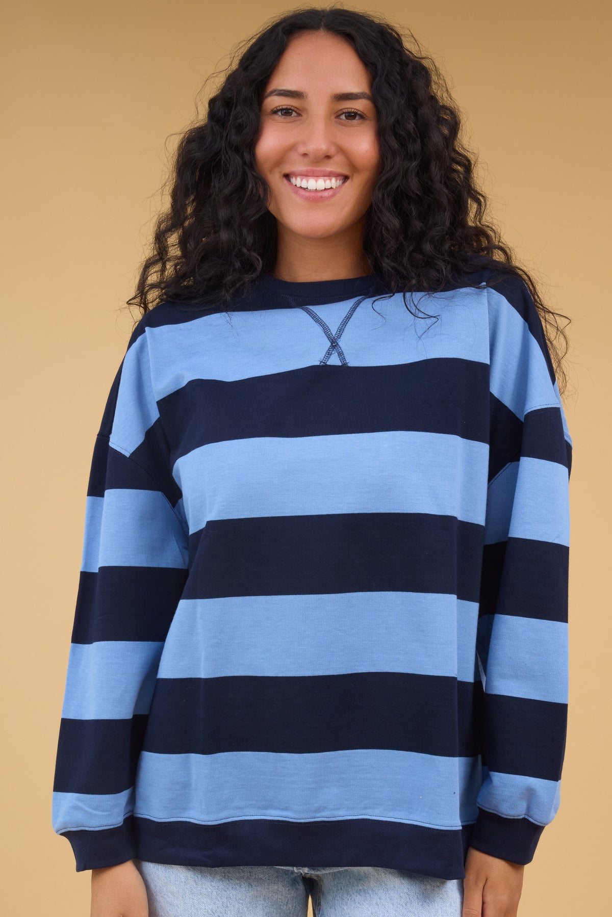 Young woman wearing a modest navy & blue wide stripe, oversized top with long sleeves.