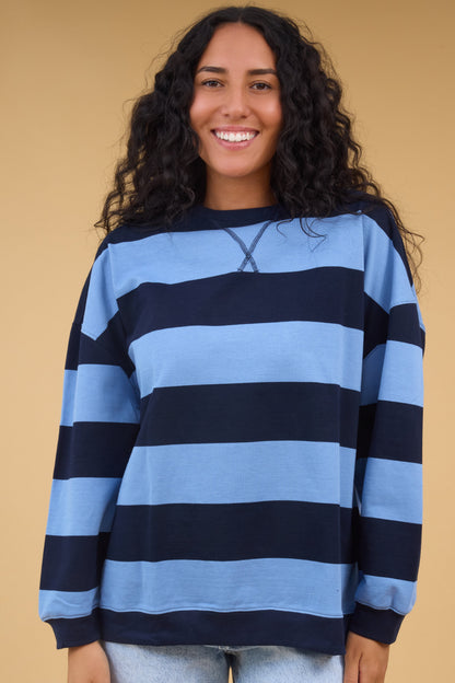 Young woman wearing a modest navy & blue wide stripe, oversized top with long sleeves.