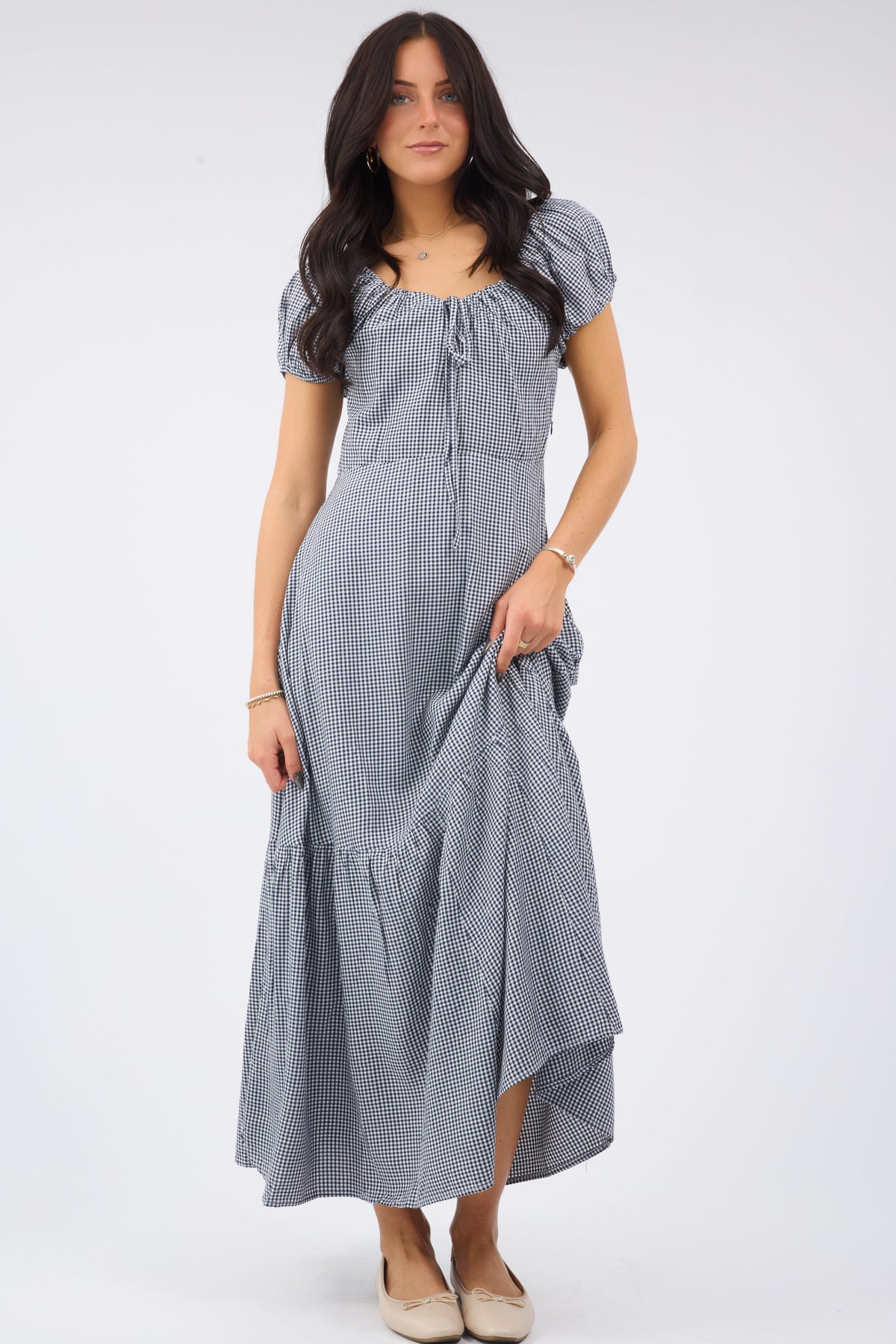 Young woman wearing a modest midi dress in navy & white gingham with a scoop neckline and short puff sleeves.