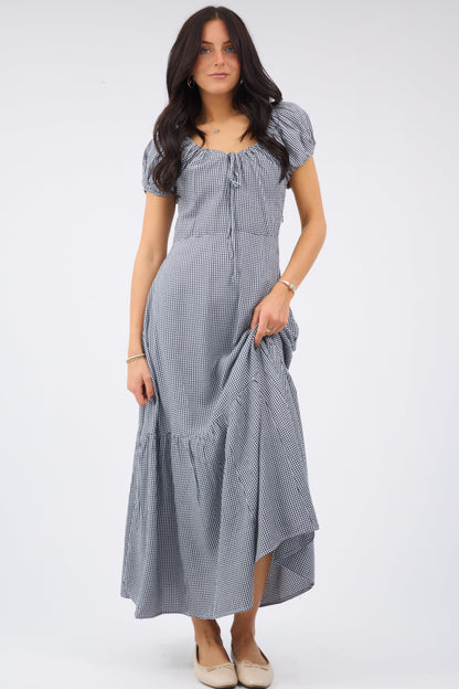 Young woman wearing a modest midi dress in navy & white gingham with a scoop neckline and short puff sleeves.
