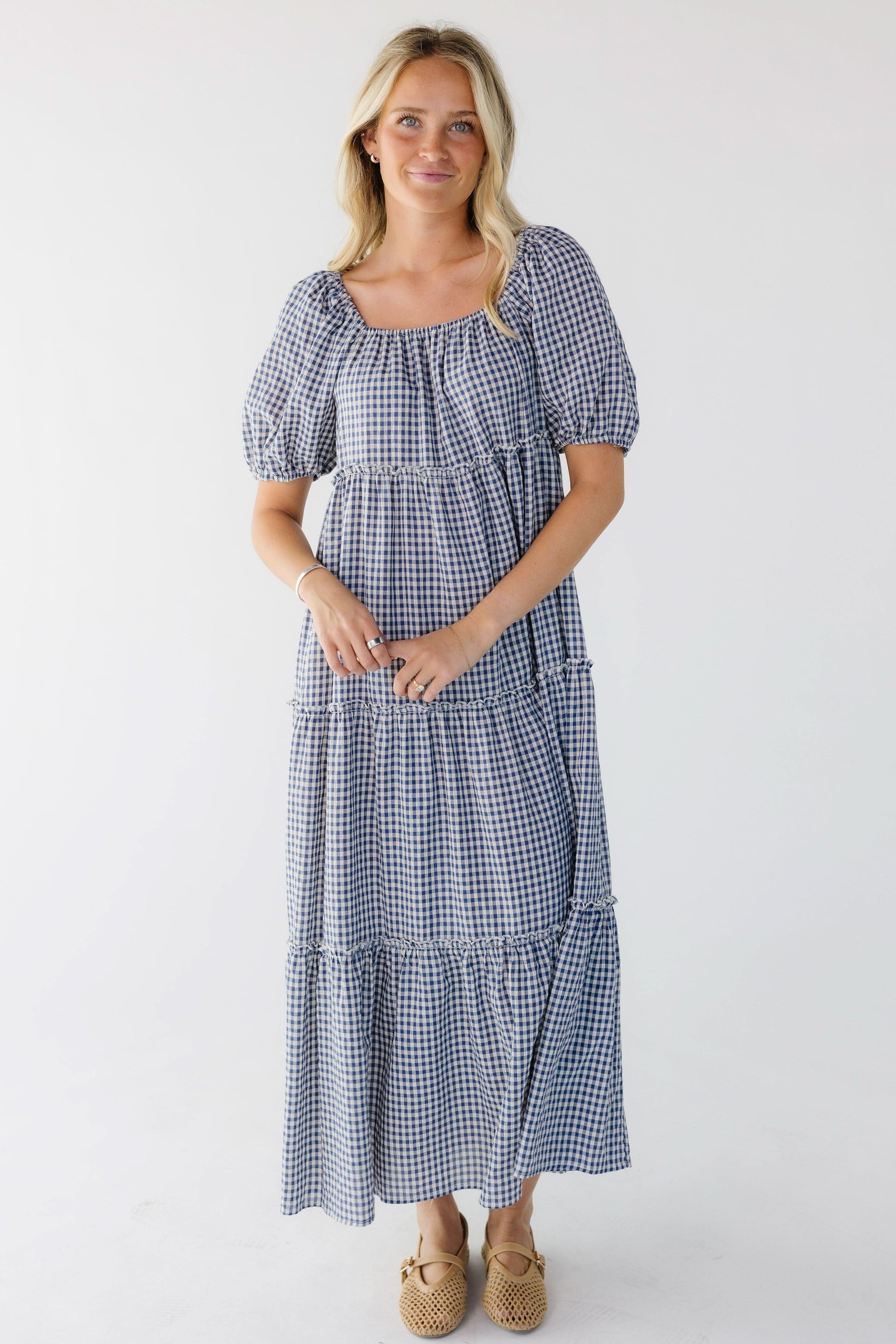Young woman wearing a blue and white gingham tiered midi skirt with balloon sleeves and a square elastic neckline.