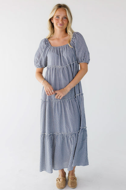 Young woman wearing a blue and white gingham tiered midi skirt with balloon sleeves and a square elastic neckline.