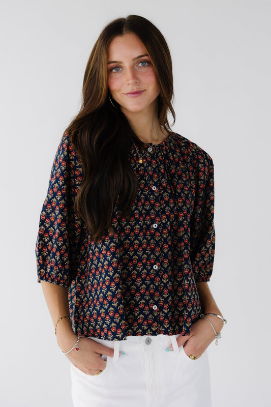 Young woman wearing a navy floral print button down blouse with elbow length sleeves and a round neckline.