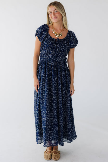 Young woman wearing a navy print midi dress with a scoop neckline, puff sleeves and a wide elastic waist.