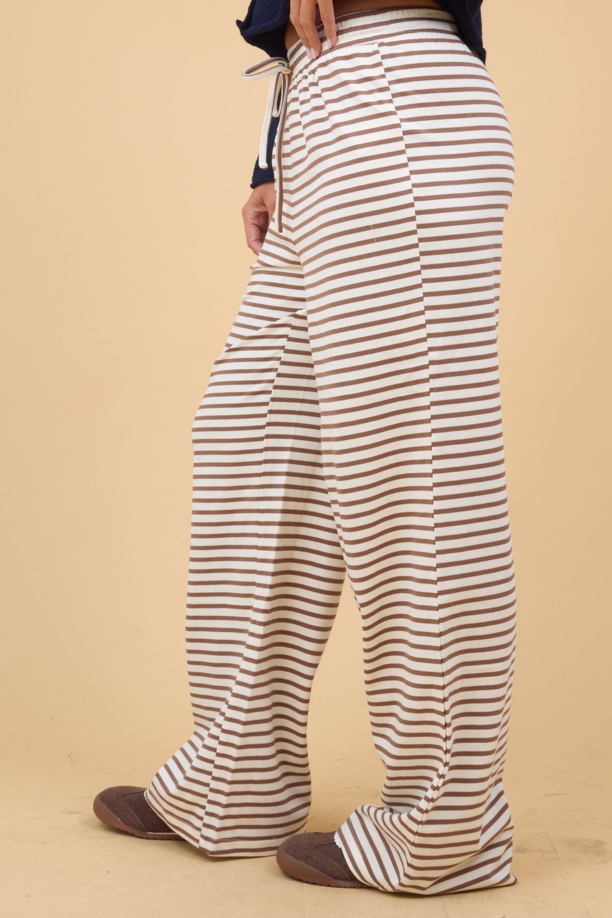 Side view of a woman wearing a pair of wide leg knit lounge pants in cream and brown stripe.
