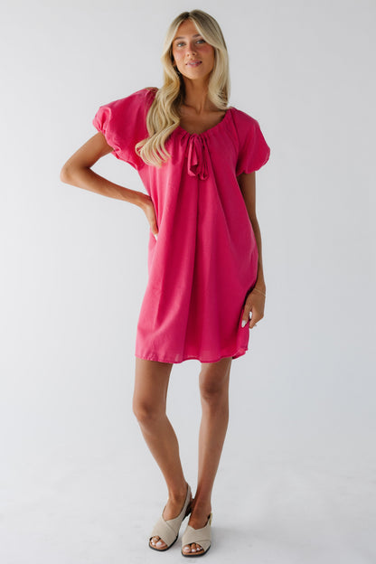 Woman wearing a pink & red gingham above the knee dress with balloon sleeves and a scoop drawstring neckline.