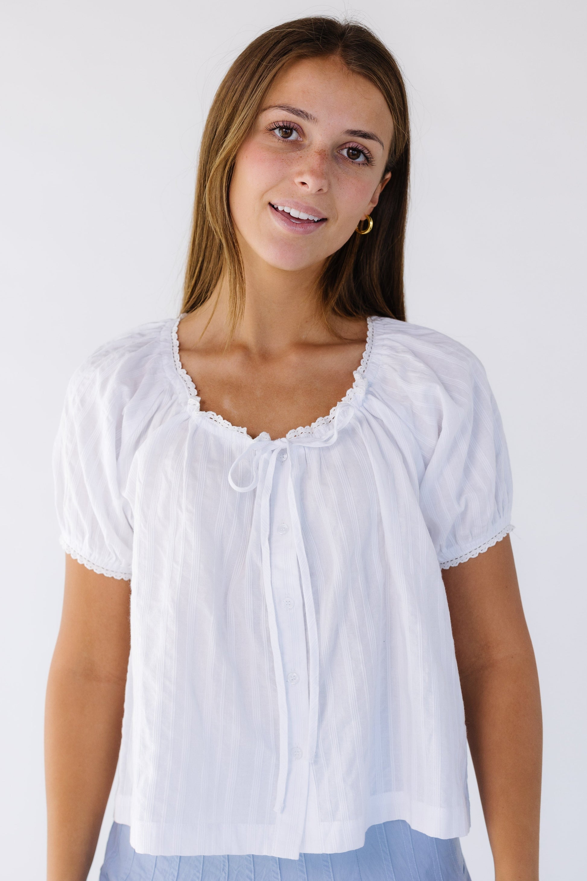 Woman wearing a white loose fitting blouse with short puff sleeves withlace trimmed necklien and sleeves.
