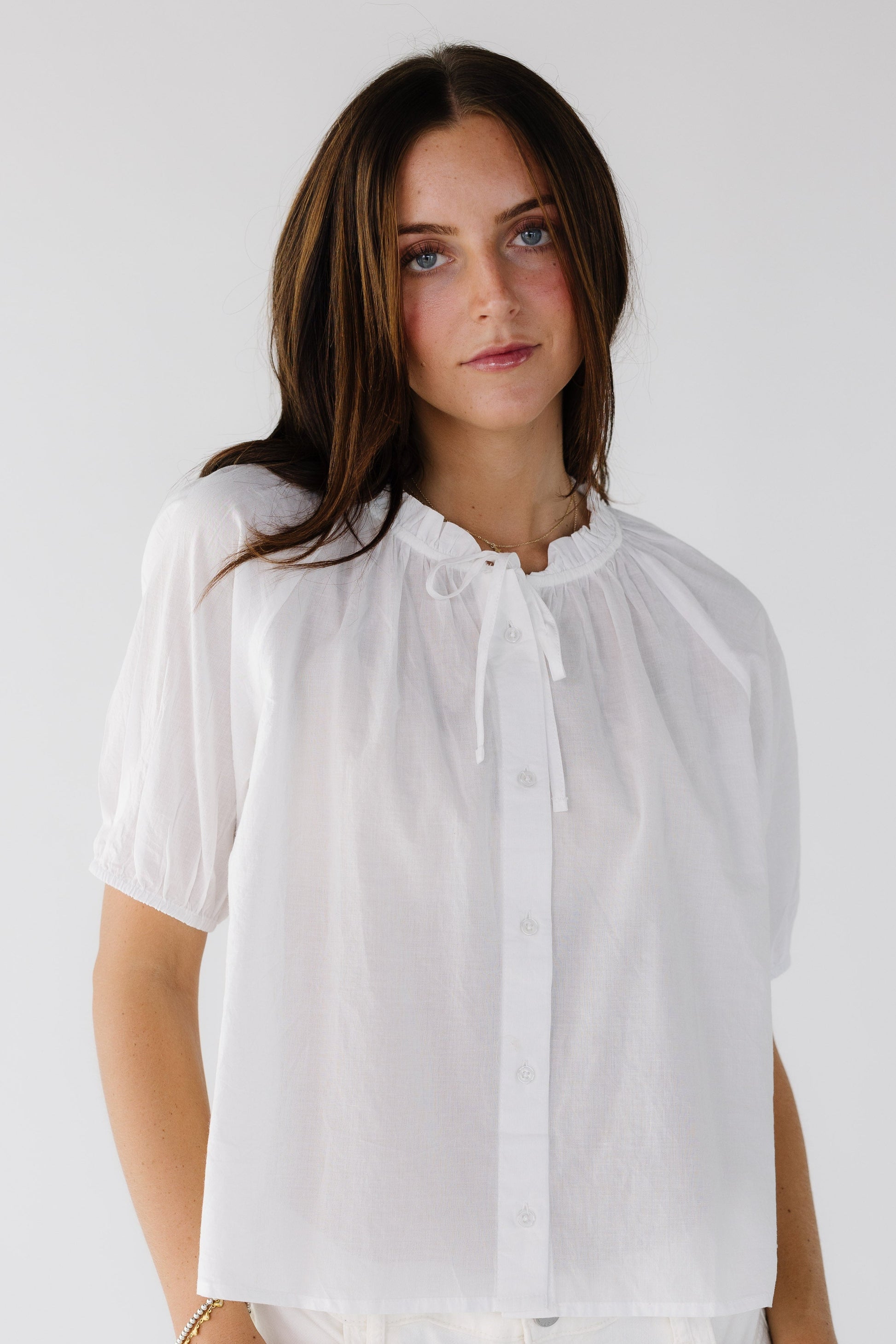 Young woman wearing a modest white button down blouse with white puff sleeves and a ruffled collar and tie.