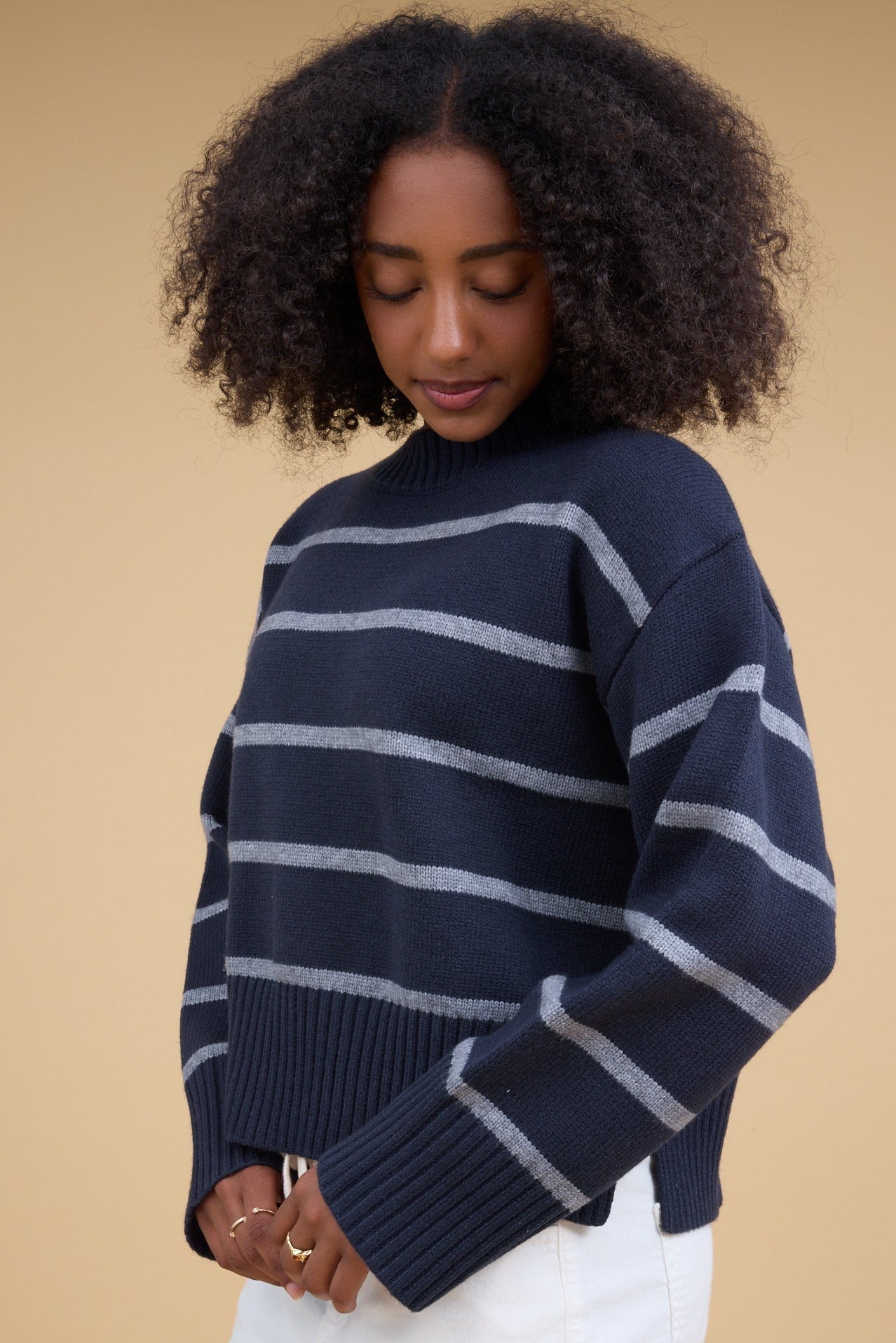 Young woman wearing a modest navy & grey stripe loose fitting pullover sweater with a wide rib knit crew neckline and long sleeves with wide, loose rib knit cuffs.