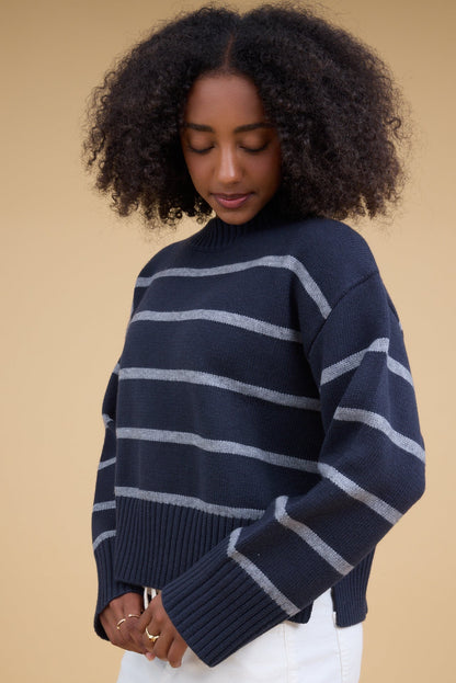 Young woman wearing a modest navy & grey stripe loose fitting pullover sweater with a wide rib knit crew neckline and long sleeves with wide, loose rib knit cuffs.