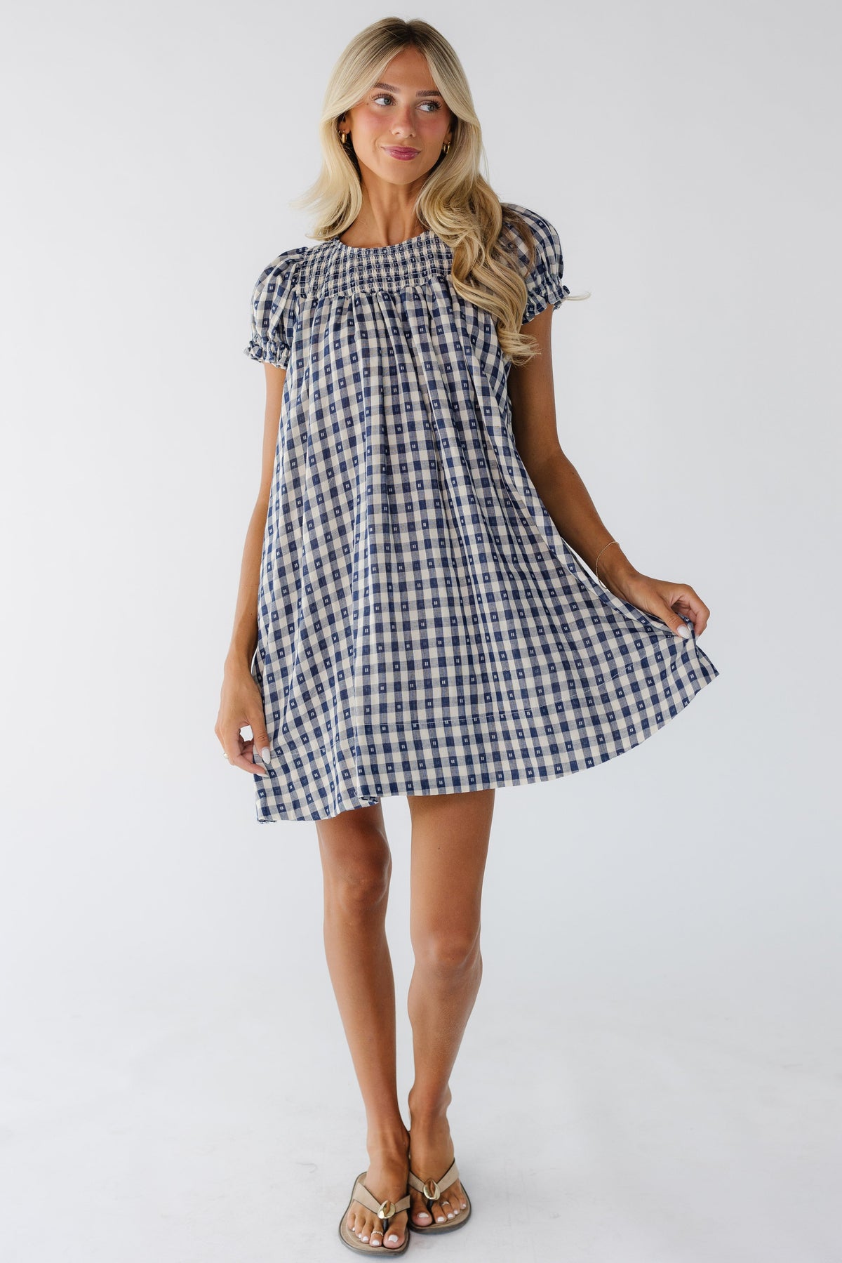 Young woman wearing a modest navy gingham babydoll dress with short puff sleeves and a smocked front yoke.