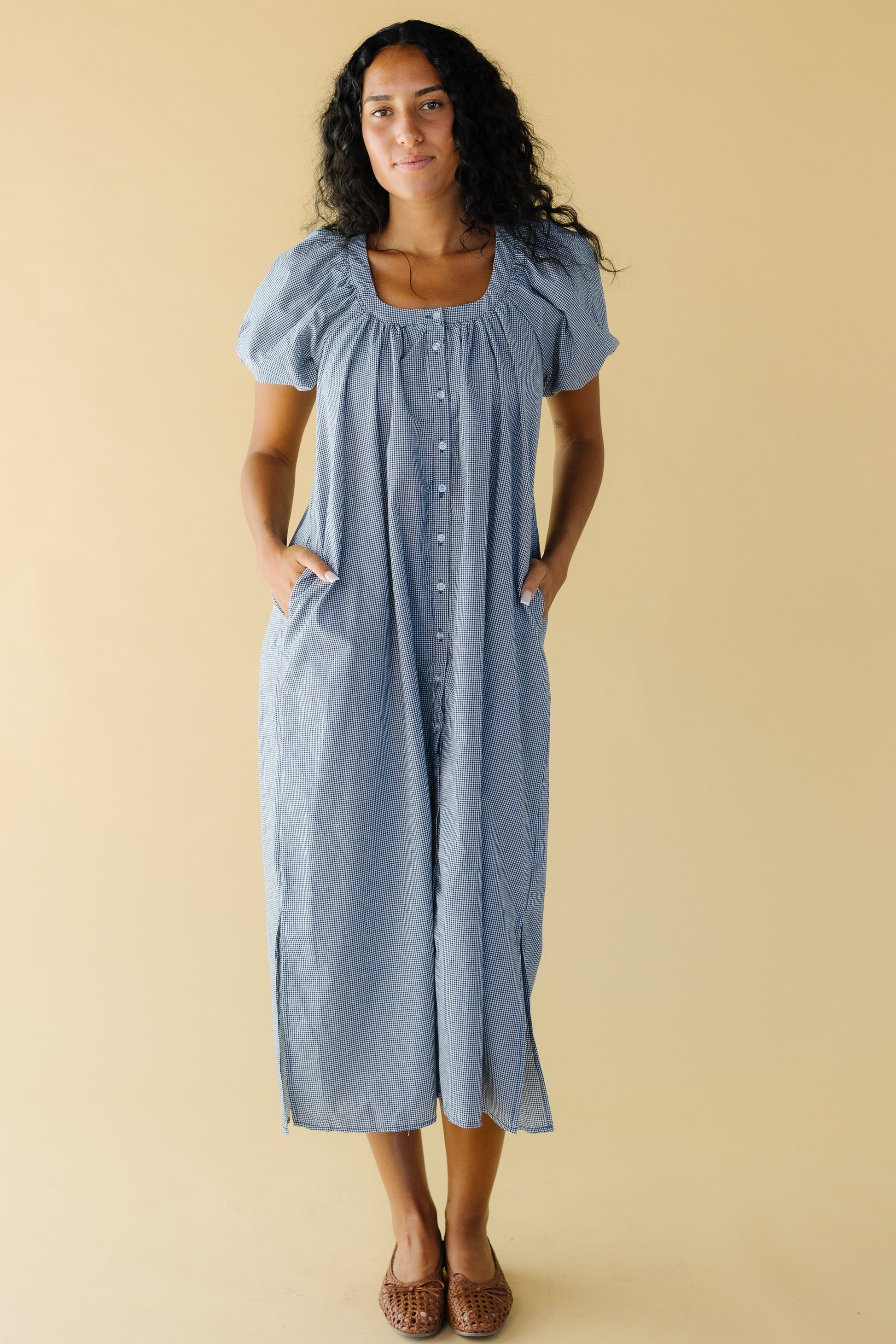 Young woman wearing a modest navy & white gingham button down midi dress with a scoop neckline, balloon sleeves and side pockets.