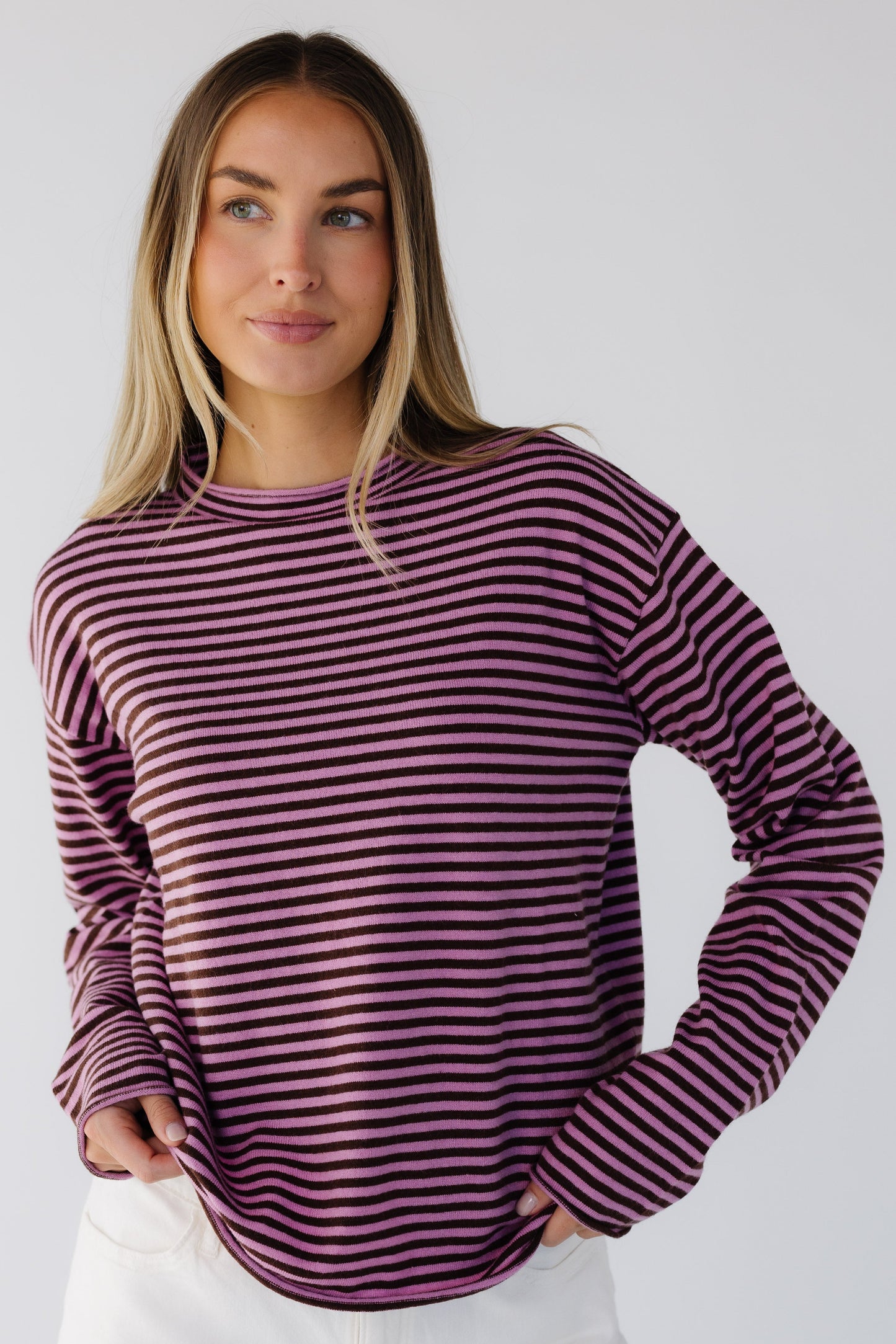 Woman wearing a pink & brown stripe lightweight knit sweater top with long sleeves and a mock turtleneck neckline.