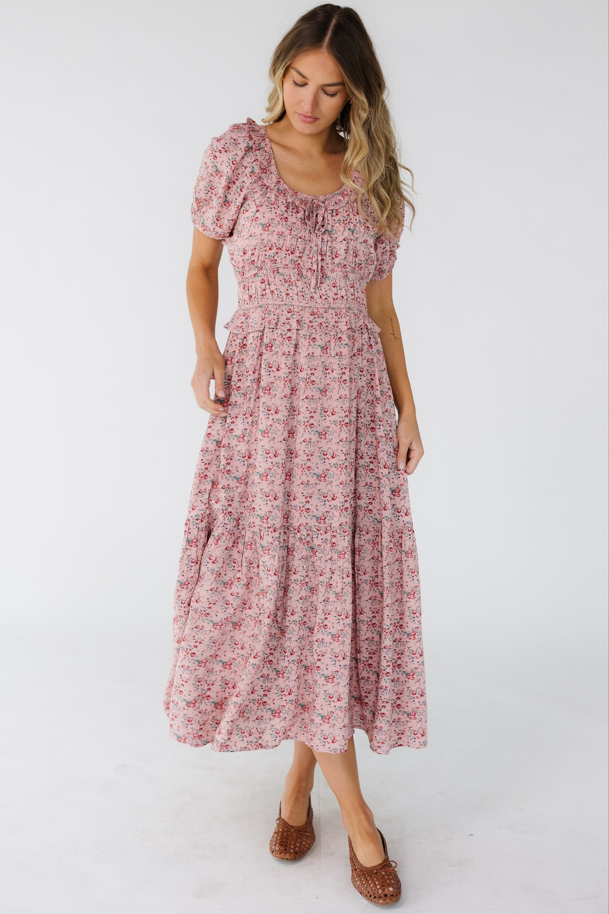 Woman wearing a pink floral print midi dress with a ruffled scoop neckline, wide elastic waistband and a wide bottom ruffle.