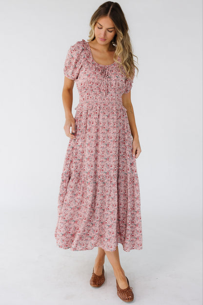 Woman wearing a pink floral print midi dress with a ruffled scoop neckline, wide elastic waistband and a wide bottom ruffle.