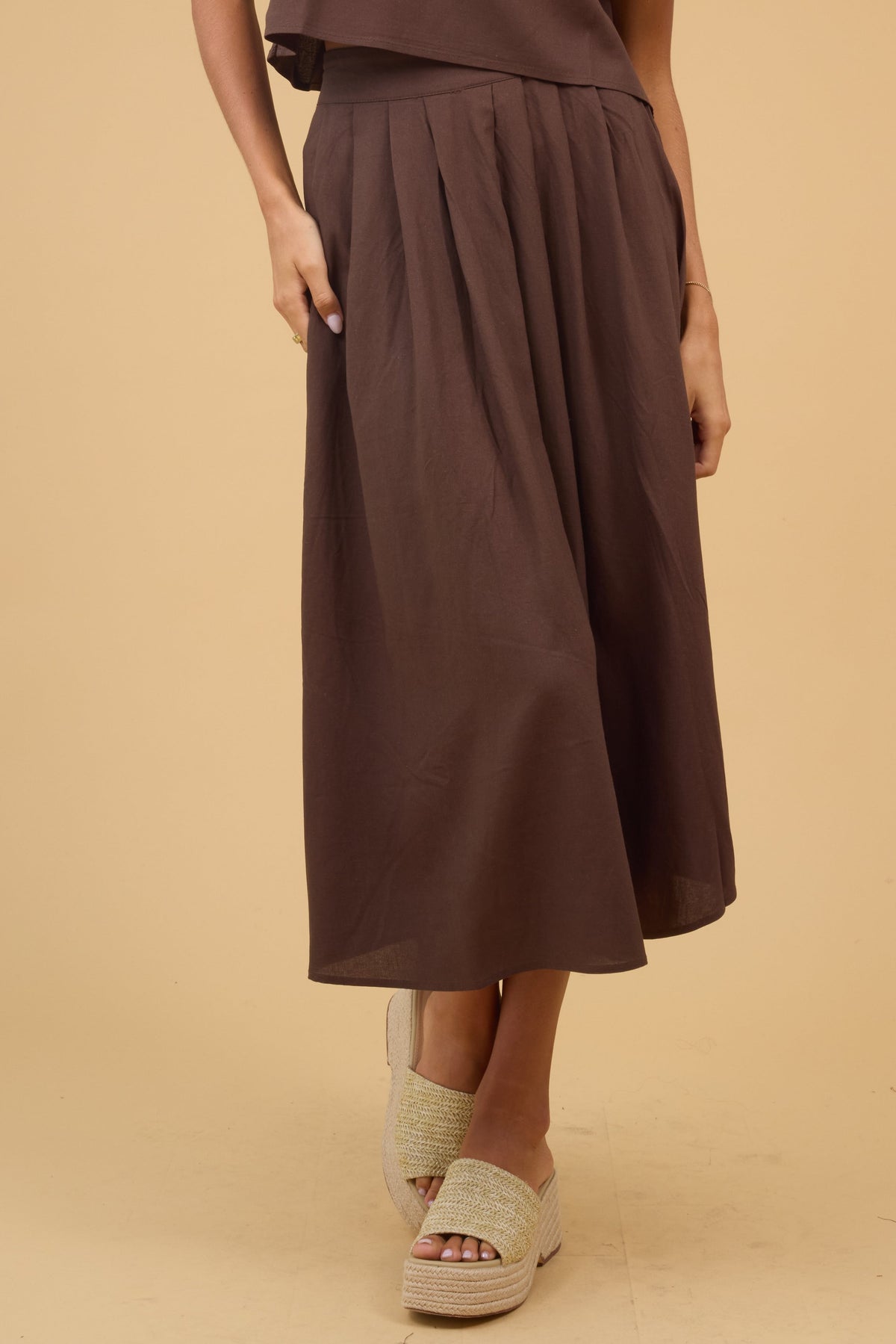Young woman wearing a brown midi skirt with front pleats and a wide waistband.
