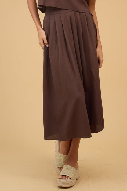 Young woman wearing a brown midi skirt with front pleats and a wide waistband.